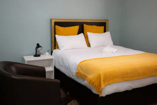 The Single Room bed with a framed headboard, a bedside table with a lamp and an armchair.