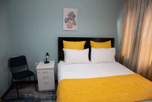 The Single Room bed seen from the foot, with a bedside table, a lamp and a chair.