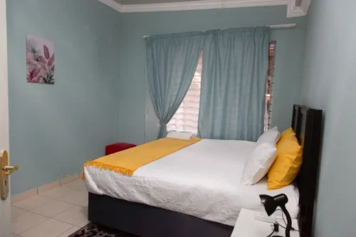 The Single Room seen from the door: a bed with a yellow throw beside the window, pale blue walls.