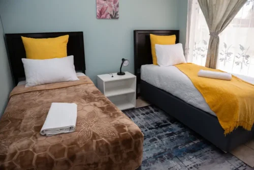 Two beds with brown and yellow throws and a bedside table between them in the Deluxe Room.