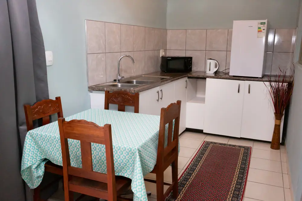 A compact kitchenette with a dining table, white refrigerator, microwave, and sink, ready for self-catering guests.